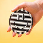 Hand holding a round black and white custom vinyl sticker patterned object against a yellow background.