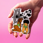 Hand holding a custom vinyl sticker with cartoon characters on a pink background.