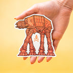 Hand holding a Star Wars AT-AT custom vinyl sticker against a yellow background.