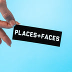 Hand holding a black custom vinyl sticker with 'PLACES+FACES' text against a light blue background.