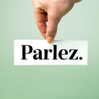 Hand holding a custom vinyl sticker with 'Parlez.' text on a light green background.