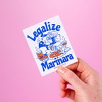 Hand holding a 'Legalize Marinara' custom vinyl sticker against a pink background.
